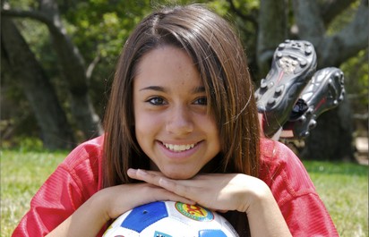 Smiling soccer player with her chin on a ball