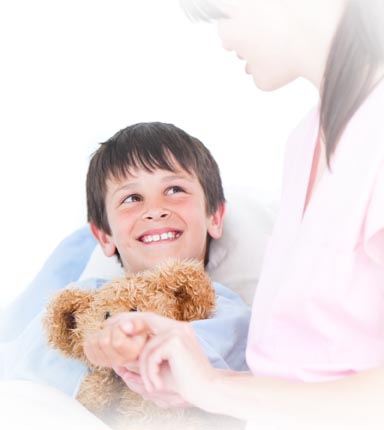 Smiling boy holding teddy bear with nurse at bedside